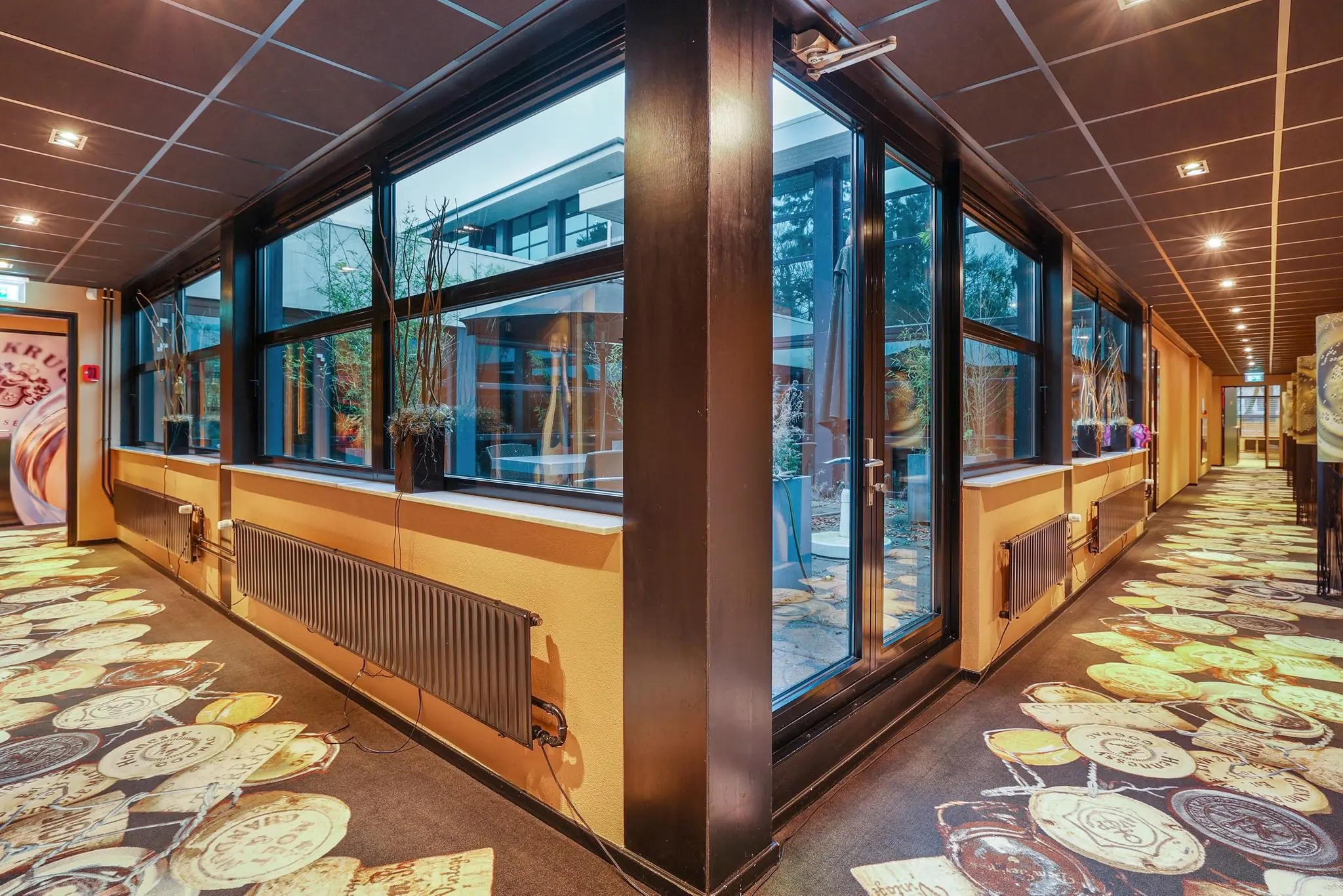 Gele betegelde gang van een modern gebouw aan de Oude Utrechtseweg met grote ramen en decoratief vloerpatroon van stempels en zegels.